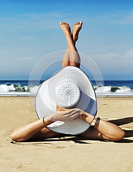 A day at the beach. Cute dainty female wearing a white two piece bikini and straw hat enjoying the sun at the beach.