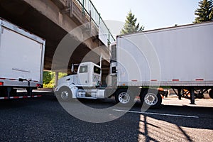 Day cab big rig semi truck going with reefer trailer with refrigeration unit under the bridge on roadside with traffic