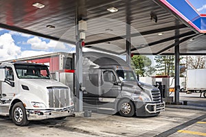 Day cab big rig semi truck and long haul gray semi truck with dry van semi trailer refuel tanks with diesel at a gas station on