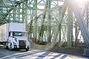 Day cab big rig white semi truck with roof spoiler transporting goods in dry van semi trailer running on the truss Columbia River