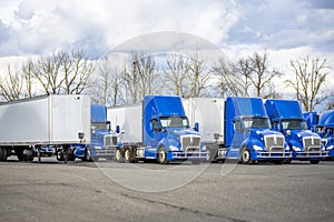 Day cab bright blue big rig semi trucks and dry van semi trailers standing in row on the industrial parking lot waiting for the