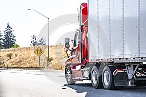 Day cab model red big rig semi truck with roof spoiler transporting cargo in dry van semi trailer running on the highway road with