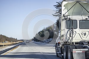 Day cab white big rig semi truck tractor with roof spoiler and without semi trailer driving on the winter divided highway road in