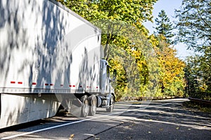 Day cab white big rig semi truck transport cargo in dry van semi trailer with aerodynamic skirt running on the autumn winding road photo