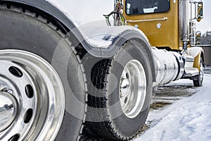 Day cab yellow big rig semi truck tractor with two driving axles and powerful wheels tires standing on the parking lot with winter