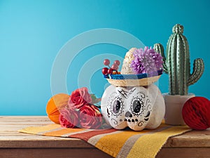 Day of the dead holiday concept. Sugar skull Halloween pumpkin and Mexican party decorations on wooden table over blue background