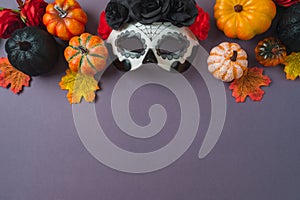 Day of the dead Mexican and Halloween holiday concept. Sugar skull mask, pumpkin and party decorations on purple background. Top