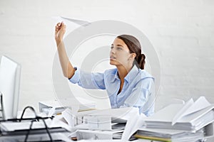 The day is just not flying fast enough. A young businesswoman throwing a paper plane while sitting at her desk.