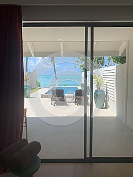A day in the Maldives, a view from the villa to sun loungers, a pool, trees and a beach on the Indian Ocean