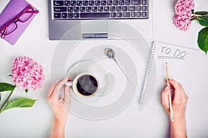 Day Planning - female hands with cup of coffee and pencil write To do list on the white working office desk with laptop, notebook,