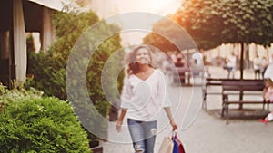 After day shopping. Young woman carrying shopping bags while walking along the street. Sunlight background