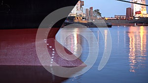 Day to night timelapse of submerged under the cargo weight freighter bow of ship into the water. Draft marks on a bulker