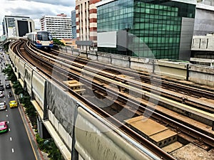 Day view of Electric Sky Train running on the rail tracks in downtown Bangkok, Thailand with ground traffic and tall buildings