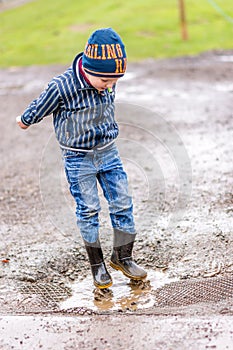 Day view excited boy jumps in a puddle