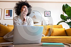 Daydreaming. African American woman using laptop working at home living room thinking. Copy space.