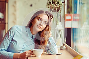 Daydreaming on a coffee break. Pensive happy woman remembering looking at side up sitting in a bar, coffee shop drinking tea