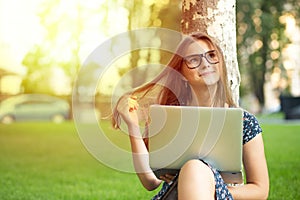 Daydreaming about future. Pensive woman teenage girl female with a laptop sitting near a tree on a green grass lawn isolated city