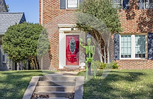 Dayglo Halloween skeleton attached to lamp post outside upscale brick house with beautiful bright red front door