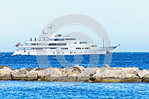 Daylight close-up view to white yacht cruising on water and splitting rocks