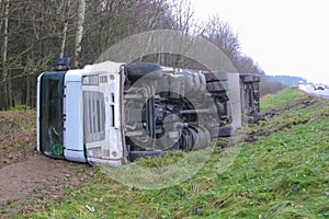 daylight. fall. A white truck with a trailer lies in a ditch turned over on its right side. Vehicle damage