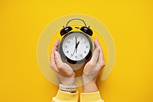 Daylight saving day. Fall Back. Black Alarm clock and female hands on yellow background. Daylight saving time end