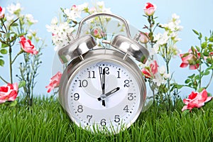 Daylight savings clock in grass with flowers spring forwards