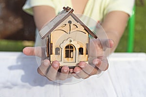 daylight. on a wooden background, in children& x27;s hands a toy house. Close-up