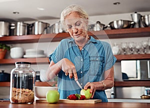 These days, she only eats healthy. an attractive senior woman chopping up apples and other fruit while preparing