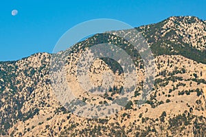 Daytime bright light of the mountains with sand cover and the moon on a blue sky