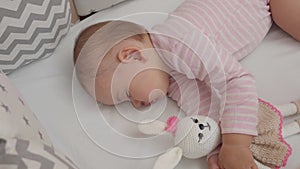 Daytime sleep. Portrait of a sleeping baby hugging a knitted bunny toy. Top view