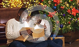 Dazed black couple opening xmas gift box in living room near Christmas tree