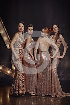 Dazzlingly beautiful girls pose in long evening dresses in the interior.