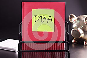 DBA text on a yellow sticker pasted on an upright diary on a black background