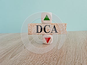 DCA symbol. A wooden cube with up icon. Brick block with the concept word DCA. Beautiful wooden table blue background. Saving