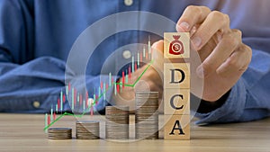 DCA word on a wooden cube and man hands holding money icon on wooden cude.Saving Coins, Saving Money.Dollar Cost Averaging