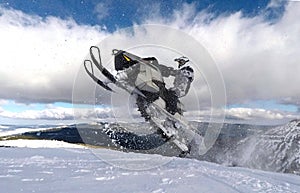 RIDER MAN WITH HELMET JUMPING WITH SNOWMOBILE BETWEEN CLOUDS ON WINTER photo