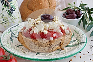 DDakos traditional Greek appetizer on a traditional plate with ceramic olive oil jar, dry rye bread, olives and olive branch. Heal