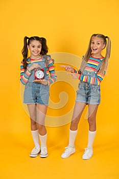 Dead line. Happy little girls hold vintage alarm clock on yellow background. Small children smiling with mechanical