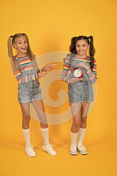Dead line. Happy little girls hold vintage alarm clock on yellow background. Small children smiling with mechanical