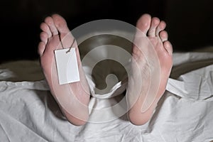 Dead man lying on the floor under white cloth with blank tag on feet - retro style