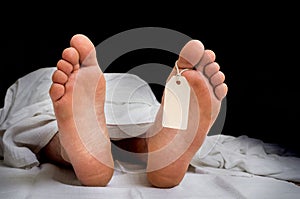 The dead man`s body with blank tag on feet under white cloth