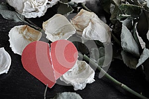 dead withered crumbling flowers roses with a red torn paper heart, as a symbol of failed love, goodbye, broken hearts, the end of