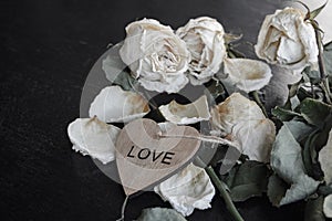 dead withered crumbling flowers roses with a wooden heart with the inscription love, as a symbol of failed love, goodbye, broken h