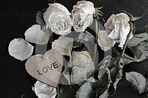 dead withered crumbling flowers roses with a wooden heart with the inscription love, as a symbol of failed love, goodbye, broken h