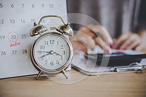 Deadline calendar for taxes payment with alarm clock on desk and blur business woman calculating