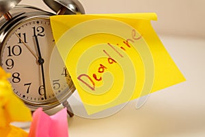 Deadline: Close-up of an alarm clock and sticky notes, emphasizing the urgency