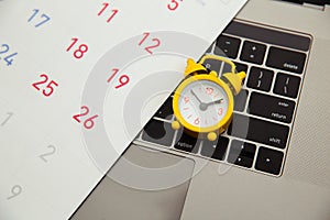 Deadline concept. Laptop and yellow alarm clock, monthly calendar on yellow background. Time is running away