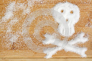 Deadly sugar addiction suggested by spilled white sugar crystals forming a skull on a wooden table