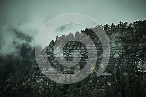 Deadpan dark misty rainy morning landscape with the sand rocky montains in Czech Saxon Switzerland in autumn colors