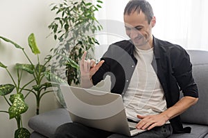 Deaf or hard hearing happy smiling young caucasian man uses sign language while video call using laptop while sitting on